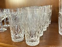 Set of 10 vintage cut crystal highball glasses arranged on wooden shelf.