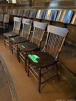 Four antique wooden chairs arranged in a row in a wooden floor interior with other seating in the background.