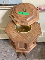 Open view showing octagonal wooden baptismal font with brass basin inside and lid lifted, hand holding lid.