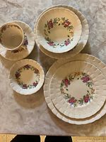 Set of bone china plates, bowls, and cups with floral pattern and textured edges.