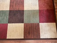 Close-up photo showing the multicolored square blocks of the carpet (red, brown, green, and cream) to highlight pattern and color condition.