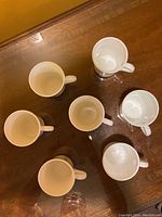 Overhead photo showing 7 of the white ceramic mugs arranged in a circle on a wooden surface, highlighting the size and shape of the mugs.