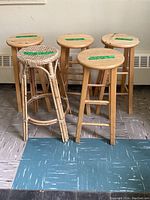 Five bar stools lined up showing four wooden stools with round seats and one wicker stool in front.