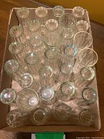 Top-down photo showing 32 clear ribbed glass juice glasses arranged side by side in a cardboard box, including 4 taller glasses.