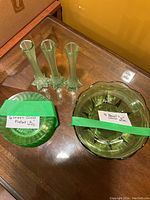Three green glass bud vases with star-shaped bases, six small green glass plates, and four green glass bowls on display on a wooden surface.