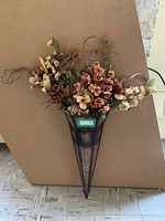 Full frontal image of metal flower wall sconce with artificial flower arrangement attached, showing colors and overall look.