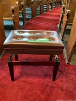 Front view of brown padded piano bench with tufted button top on red carpet aisle.