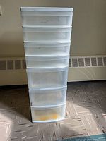 Seven drawer white storage tower with clear drawers standing upright on floor.