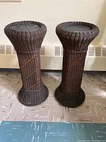 Full view of two wicker plant stands showing their hourglass shape and dark brown woven wicker construction.