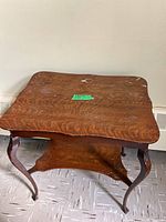 View of the wooden two-tiered table showing the scalloped edge top and curved decorative legs from a higher perspective.