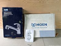 Two unopened boxes containing new kitchen faucets - Zurn and Moen brands