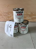 Three unopened metal cans of Tremclad Red Oxide Rust Paint Primer stacked in a pyramid shape against a wooden backdrop.