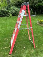 Side view of red fiberglass step ladder with aluminum steps on grass.