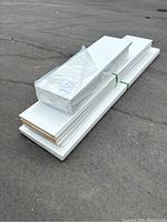 Photo showing stacked white foam insulation sheets of varying sizes strapped together on asphalt surface.
