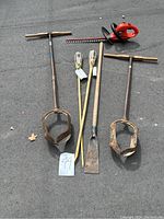 Full view of garden and automotive tools showing two post hole diggers, tiki torches, hedge clipper, ice scraper on asphalt surface