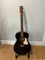 Full front view of faded black acoustic guitar on stand.