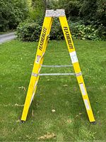 Front view of yellow Featherlite fiberglass ladder on grass showing the two sided steps and Featherlite branding on side rails.