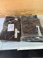 Two stacks of ten individually packaged dark grey men's tactical pants by Propper, size 34x36, displayed on a white table.