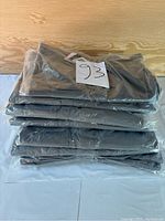 Plastic-wrapped stack of 10 folded grey tactical pants on table with lot number 93.