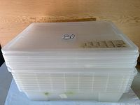 Stack of 8 clear plastic totes with lids on top, showing side profile and ribbed design.