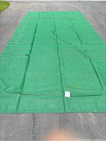 Full view of green mesh tarp laid flat on pavement showing size and condition.