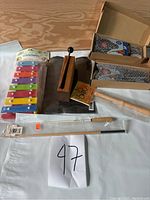 Top view of a colorful 8-tone glockenspiel, wooden percussion block with striker, and several drumsticks and mallets all arranged on a wooden surface with a paper '97' note.