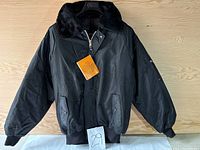 Front view of black bomber winter coat with removable black fur-like collar and ribbed hem and cuffs, showing Canada Sportswear tag attached to zipper.