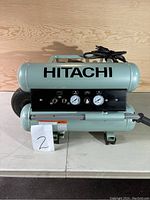 Front view of the portable Hitachi air compressor showing dual tanks, control panel with gauges and hose connectors.