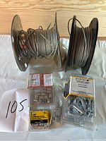 Two spools of galvanized steel cable with packages of wire rope fittings including sleeves, thimbles, and clips arranged in front.