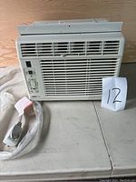 Front view of the white UBERHAUS window air conditioner, showing ventilation grill, control panel, and attached power cord.