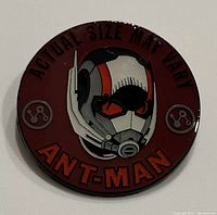 Front of the circular Ant Man collector's pin with red background and helmet design, featuring text 'Actual Size May Vary' and 'Ant-Man'.