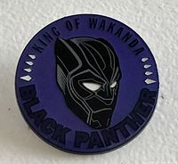 Front view of the circular Marvel Disney Black Panther collector's pin showing mask and text on purple background.