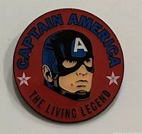 Front view of circular Captain America pin with red background, masked head illustration and text.