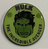 Front view of round green enamel pin showing Hulk's face and text.