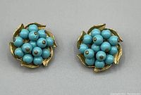 Pair of gold tone and turquoise beaded clip-on earrings shown on a light grey surface. The circular cluster bead design with gold tone leaves is clearly visible. Photo taken to show condition and design details.