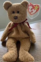 Front view of the rare retired Ty Beanie Baby "Curly" sitting upright, showing its soft fur texture, eyes, nose, and red ribbon around its neck, including the original heart-shaped Ty tag attached.