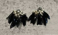 Photo of the pair of vintage black bead and faux pearl dangle clip on earrings laid flat on a grey background, showing bead fringe and pearl clusters.