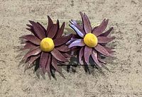 Photo showing a pair of vintage purple and yellow wooden earrings shaped like flowers, displayed on a grey textured background.