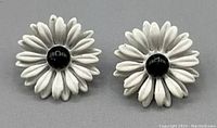 Pair of white and black floral daisy shaped stud earrings with white petals and black centers on a plain white background.