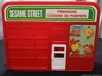 Front view of the 1980's Sesame Street Firehouse playset with a white door and colorful decal featuring Bert and Ernie dressed as firefighters.