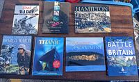 Photo of 7 coffee table books mainly on World War II, Titanic, art, and history topics displayed on a wooden bench.