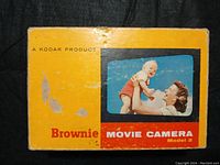 Yellow Kodak Brownie Movie Camera Model 2 box with image of woman holding child, showing surface wear and scuffs.