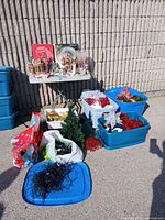 Wide view showing all items in the lot including the small artificial tree, bins, lights, ornaments, and village set on a folding table