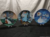Wide shot showing all three Cinderella decorative plates on stands against a neutral cloth background.