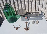 Overview of vintage scale, green glass bottle, cast iron animal coat hanger hooks, and two small scale weights on a white surface against a brick background.