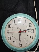 Front view of the vintage Ingraham electric wall clock with an atomic blue round frame and white clock face.