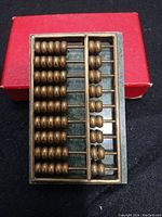 Top view of a small decorative abacus with brass beads, showing the red box in the background.