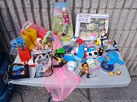 Full lot displayed on table outdoors showing toys, doll in box, tea set, novelty boots, and various small collectibles.