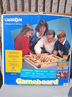 Front of Carrom gameboard box featuring family playing the game and branding information