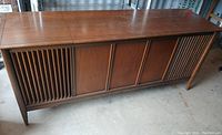 Full view of the vintage wooden record album player console with vertically slatted side speaker covers and medium brown finish.